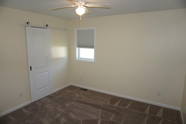 empty room with dark carpet, a barn door, and a ceiling fan