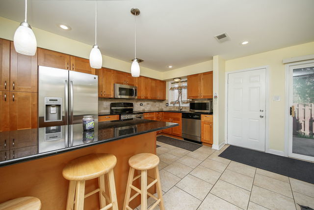 1S215 Stratford Ln, Villa Park, IL 60181 - kitchen with appliances with stainless steel finishes, brown cabinetry, dark countertops, a kitchen breakfast bar, and decorative backsplash