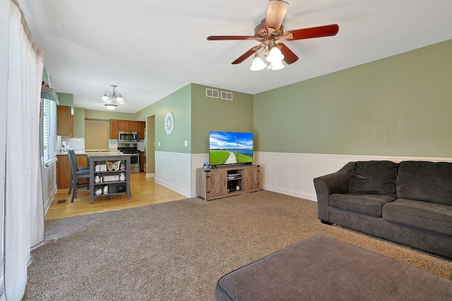 710 Cimarron Dr, Cary, IL 60013 - living area featuring light carpet, a wainscoted wall, a ceiling fan, and a chandelier