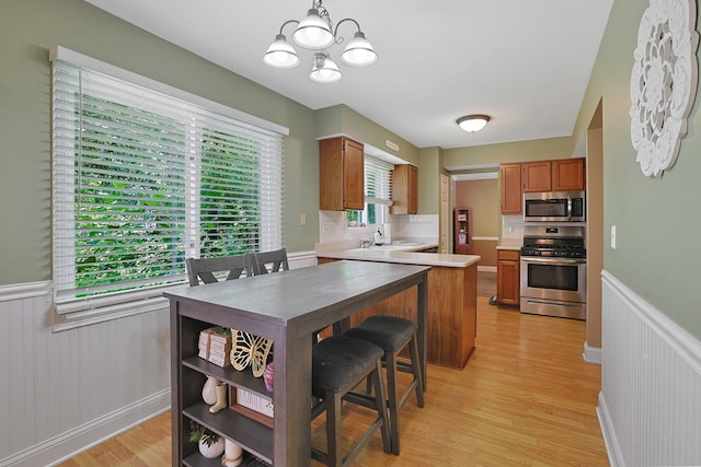 710 Cimarron Dr, Cary, IL 60013 - kitchen with appliances with stainless steel finishes, a chandelier, light countertops, a wainscoted wall, and light wood finished floors