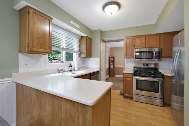 710 Cimarron Dr, Cary, IL 60013 - kitchen featuring stainless steel appliances, a peninsula, light countertops, decorative backsplash, and brown cabinetry