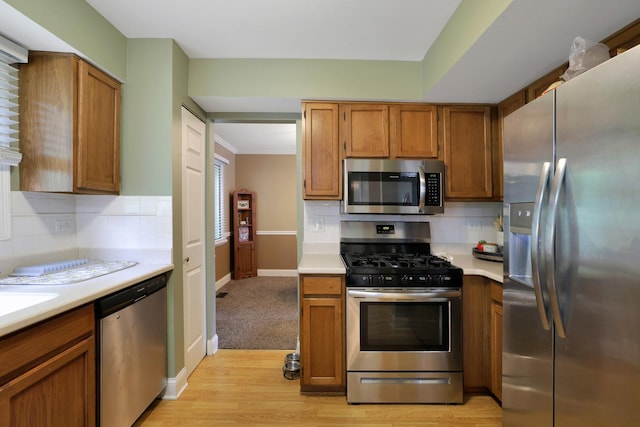 710 Cimarron Dr, Cary, IL 60013 - kitchen featuring stainless steel appliances, light countertops, tasteful backsplash, brown cabinets, and light wood finished floors