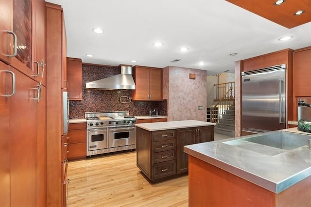 8850 Karlov Ave, Skokie, IL 60076 - kitchen with premium appliances, wall chimney range hood, stainless steel countertops, a kitchen island, and light wood-style floors