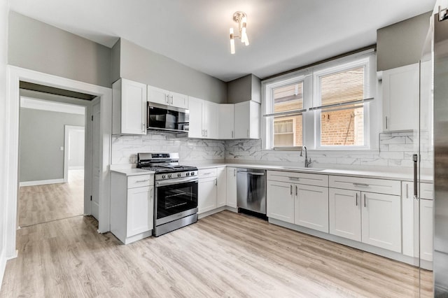 8510 S Blackstone Ave, Chicago, IL 60619 - kitchen featuring appliances with stainless steel finishes, light countertops, backsplash, light wood-type flooring, and white cabinetry