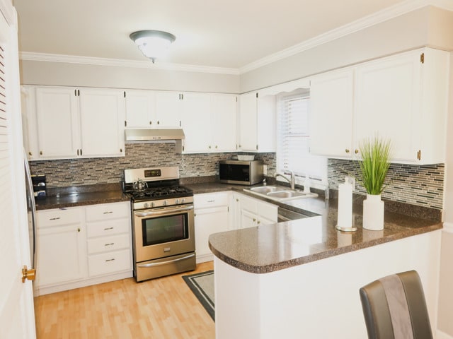 2545 N 72nd Ct Unit 4, Elmwood Park, IL 60707 - kitchen with stainless steel appliances, under cabinet range hood, a peninsula, white cabinetry, and crown molding