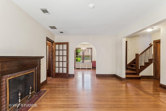 733 N Kensington Ave, La Grange Park, IL 60526 - unfurnished living room featuring light wood-style flooring, stairs, a fireplace with flush hearth, arched walkways, and a chandelier