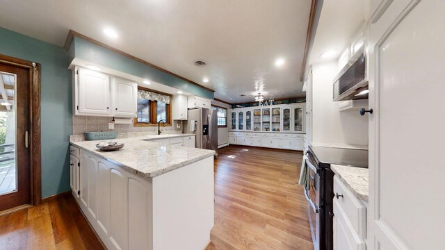 17 Park Dr, Villa Grove, IL 61956 - kitchen with appliances with stainless steel finishes, white cabinets, a peninsula, backsplash, and light wood-style floors