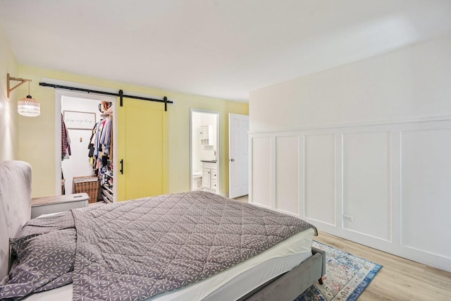 1521 S County Farm Rd Unit 2-2, Wheaton, IL 60189 - bedroom with a barn door, a decorative wall, light wood finished floors, connected bathroom, and wainscoting