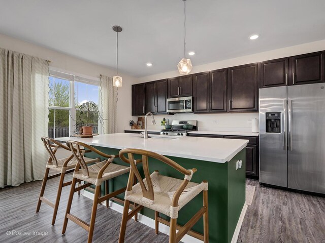 257 Kennedy Dr, Saint Charles, IL 60175 - kitchen with stainless steel appliances, a kitchen island with sink, wood finished floors, light countertops, and a breakfast bar