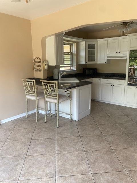 10900 S Tripp Ave, Oak Lawn, IL 60453 - kitchen with under cabinet range hood, dark countertops, black microwave, a kitchen bar, and white cabinetry