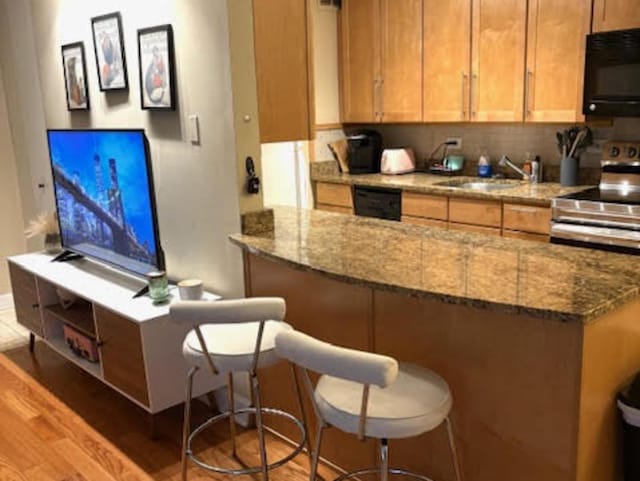 1339 N Dearborn St Unit 4A, Chicago, IL 60610 - kitchen with black appliances, light wood-style flooring, a breakfast bar area, stone countertops, and brown cabinets