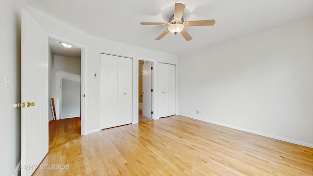 unfurnished bedroom with light wood finished floors, a ceiling fan, and multiple closets