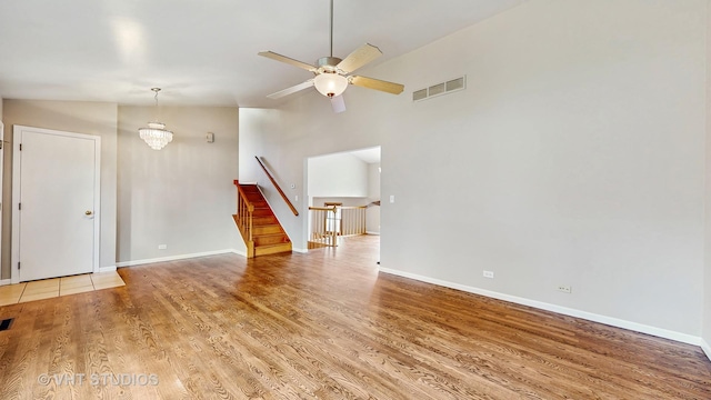 unfurnished living room with light wood-type flooring, a ceiling fan, a chandelier, stairs, and high vaulted ceiling