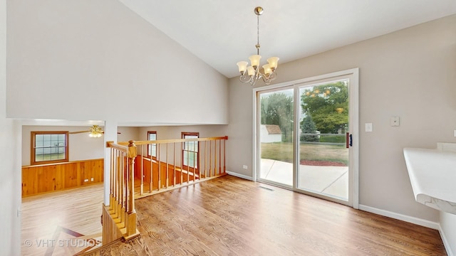 unfurnished room featuring a chandelier, wood finished floors, ceiling fan, high vaulted ceiling, and wooden walls