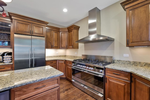 18013 Saint Andrews Dr, Marengo, IL 60152 - kitchen featuring stainless steel appliances, wall chimney exhaust hood, dark wood finished floors, light stone countertops, and brown cabinetry