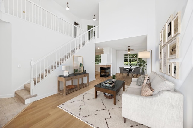 2566 Camberley Cir, Westchester, IL 60154 - living room with stairway, a ceiling fan, wood finished floors, a towering ceiling, and a tiled fireplace