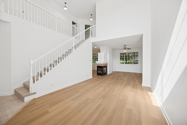 2566 Camberley Cir, Westchester, IL 60154 - unfurnished living room with stairway, ceiling fan, light wood-style floors, a towering ceiling, and a tiled fireplace