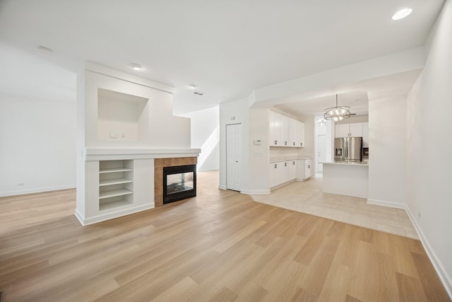 2566 Camberley Cir, Westchester, IL 60154 - unfurnished living room with a tiled fireplace, light wood-type flooring, a chandelier, and built in shelves