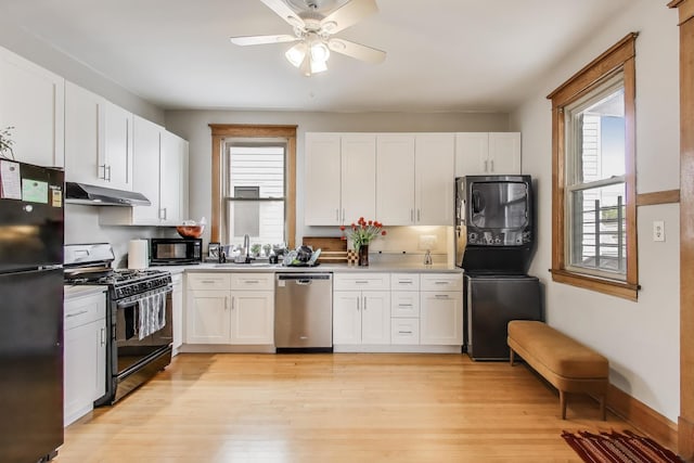 2333 N Spaulding Ave, Chicago, IL 60647 - kitchen featuring black appliances, stacked washer and clothes dryer, under cabinet range hood, white cabinetry, and light wood finished floors