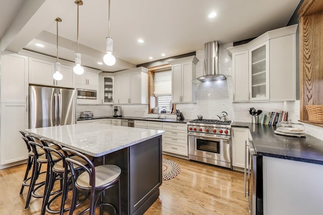 2333 N Spaulding Ave, Chicago, IL 60647 - kitchen featuring stainless steel appliances, wall chimney exhaust hood, a kitchen breakfast bar, a kitchen island, and light wood finished floors
