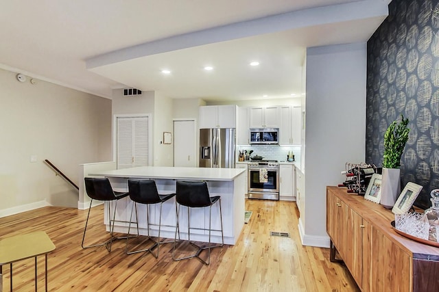2136 W Schiller St Unit 1R, Chicago, IL 60622 - kitchen featuring appliances with stainless steel finishes, a kitchen island, light wood-style flooring, a breakfast bar area, and white cabinetry