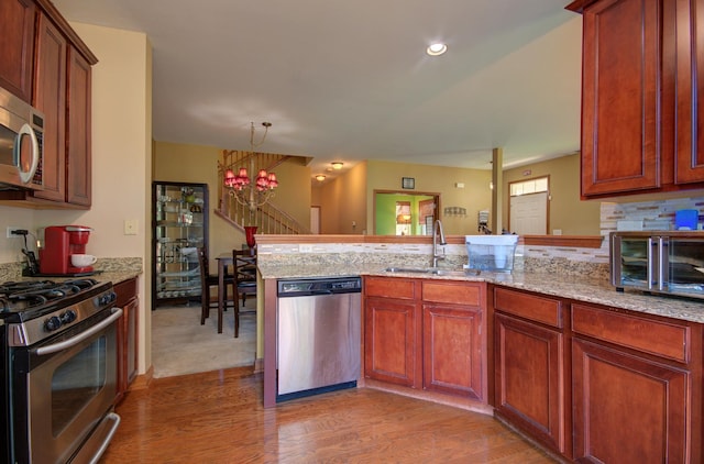 381 Chesapeake Ln, Oswego, IL 60543 - kitchen featuring stainless steel appliances, a peninsula, a chandelier, light wood-type flooring, and light stone countertops