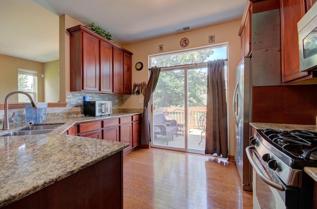 381 Chesapeake Ln, Oswego, IL 60543 - kitchen with appliances with stainless steel finishes, light wood-style floors, light stone countertops, tasteful backsplash, and reddish brown cabinets