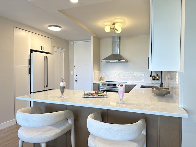720 W Gordon Ter Unit 6J, Chicago, IL 60613 - kitchen featuring wall chimney exhaust hood, high end fridge, a peninsula, and a breakfast bar
