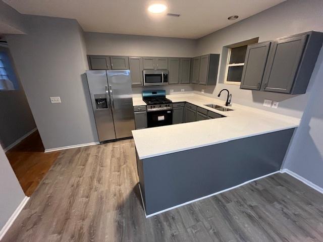 1352 S Kedvale Ave, Chicago, IL 60623 - kitchen with stainless steel appliances, gray cabinetry, a peninsula, light countertops, and wood finished floors