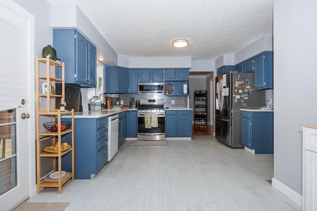 3308 Cumbria Dr, Bloomington, IL 61704 - kitchen with stainless steel appliances, blue cabinets, decorative backsplash, light countertops, and a textured ceiling