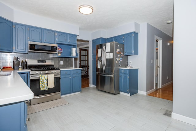 3308 Cumbria Dr, Bloomington, IL 61704 - kitchen featuring appliances with stainless steel finishes, blue cabinetry, tasteful backsplash, and light countertops