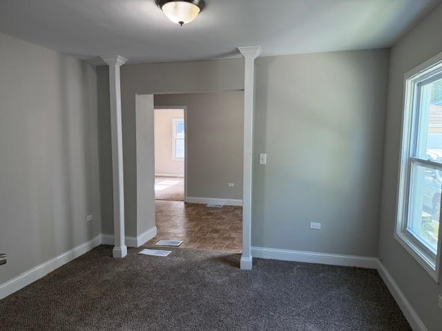 1023 N Elmwood Ave, Waukegan, IL 60085 - spare room featuring ornate columns, healthy amount of natural light, and dark carpet