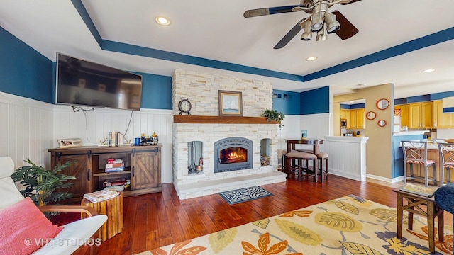 25333 W Richmond Ave, Antioch, IL 60002 - living room featuring wainscoting, a tray ceiling, ceiling fan, hardwood / wood-style flooring, and a stone fireplace