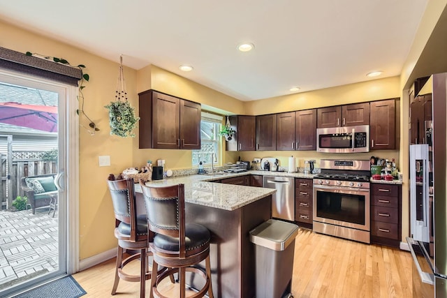 5404 N Hoyne Ave Unit 5404, Chicago, IL 60625 - kitchen with stainless steel appliances, a peninsula, dark brown cabinets, light stone countertops, and a breakfast bar area
