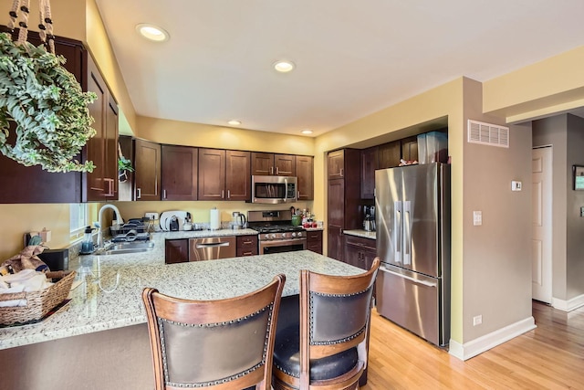 5404 N Hoyne Ave Unit 5404, Chicago, IL 60625 - kitchen with appliances with stainless steel finishes, a peninsula, dark brown cabinetry, light stone counters, and light wood-style flooring