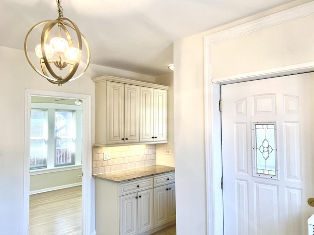 2614 W Lunt Ave, Chicago, IL 60645 - kitchen featuring a chandelier, backsplash, light wood-type flooring, light stone counters, and hanging light fixtures
