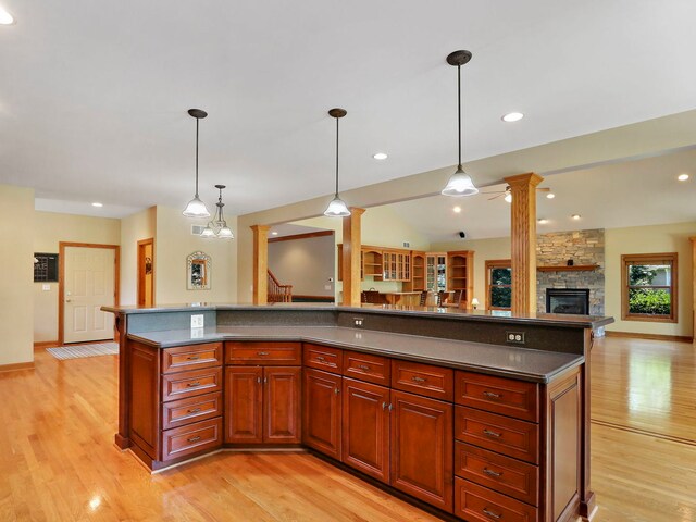 9804 Palmer Dr, Lakewood, IL 60014 - kitchen with ornate columns, light wood-type flooring, dark countertops, a stone fireplace, and pendant lighting