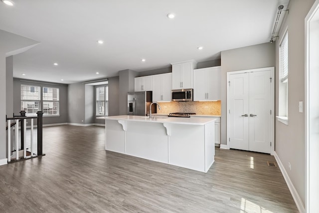 10606 Paige Ct, Orland Park, IL 60462 - kitchen with stainless steel appliances, a kitchen island with sink, light countertops, light wood-type flooring, and white cabinets