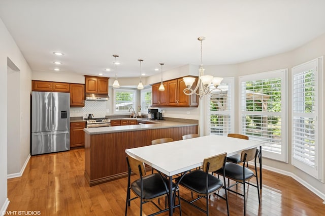 1460 Canter Ln, Bartlett, IL 60103 - kitchen featuring stainless steel appliances, light wood finished floors, a chandelier, under cabinet range hood, and brown cabinetry