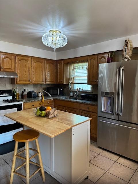14240 S Manistee Ave, Burnham, IL 60633 - kitchen featuring stainless steel appliances, butcher block countertops, under cabinet range hood, light tile patterned floors, and a chandelier