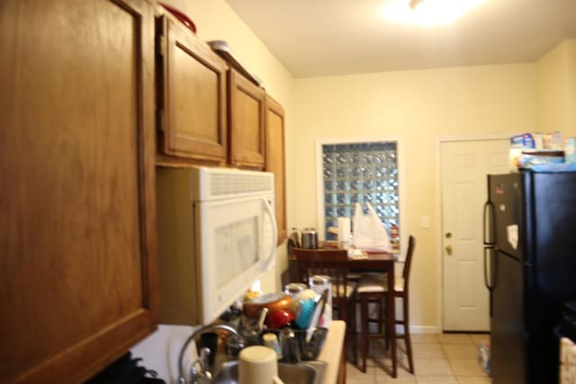 6948 S Eberhart Ave, Chicago, IL 60637 - kitchen featuring freestanding refrigerator, white microwave, brown cabinets, and light tile patterned flooring