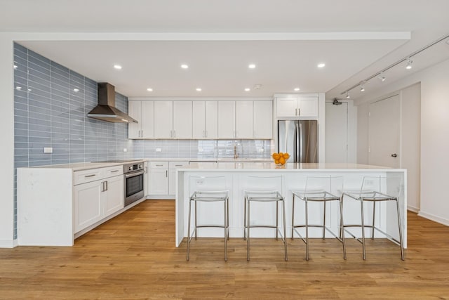 330 W Diversey Pkwy Unit 2306, Chicago, IL 60657 - kitchen featuring wall chimney range hood, stainless steel appliances, a breakfast bar, white cabinets, and decorative backsplash