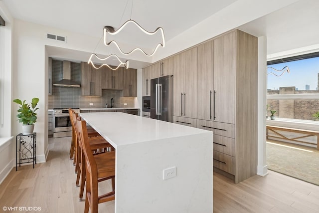 1261 N Paulina Ave Unit 6, Chicago, IL 60622 - kitchen featuring stainless steel appliances, modern cabinets, wall chimney range hood, a breakfast bar area, and light wood finished floors