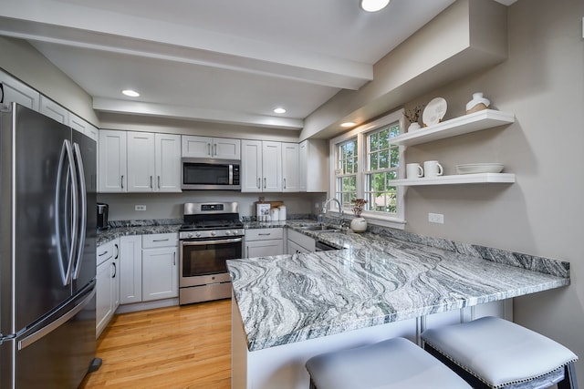 74 White Oak Cir, Saint Charles, IL 60174 - kitchen featuring appliances with stainless steel finishes, a peninsula, light wood-style flooring, light stone countertops, and a breakfast bar