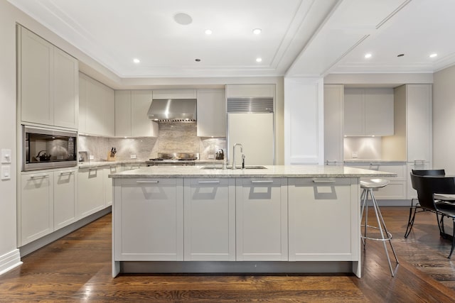 159 E Walton Pl Unit 5C, Chicago, IL 60611 - kitchen featuring wall chimney range hood, built in appliances, crown molding, tasteful backsplash, and a kitchen island with sink