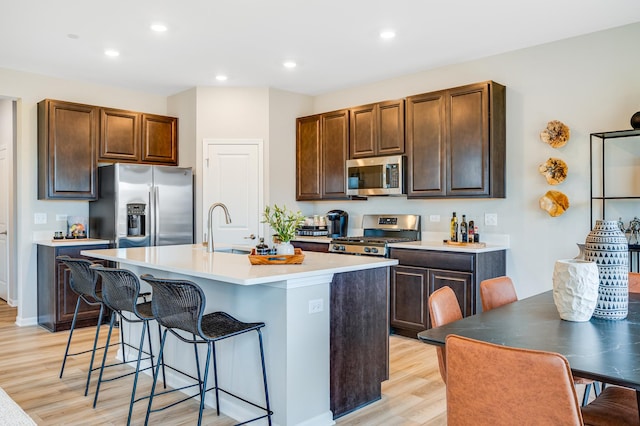 12124 Kelsey Dr, Huntley, IL 60142 - kitchen with appliances with stainless steel finishes, a breakfast bar area, light wood-style floors, a center island with sink, and light countertops