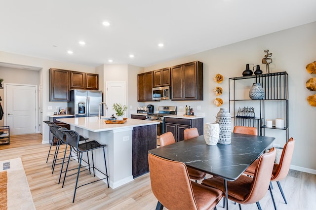 12124 Kelsey Dr, Huntley, IL 60142 - kitchen with appliances with stainless steel finishes, a breakfast bar area, light wood-style floors, a center island with sink, and recessed lighting
