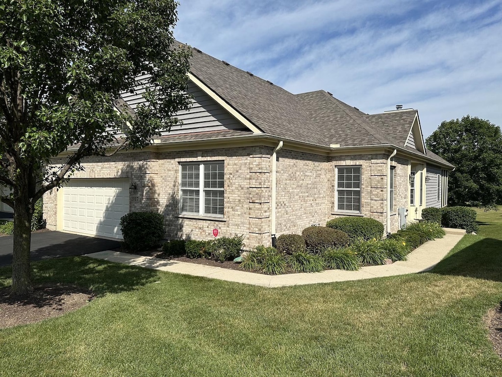 2017 Mallard Ln, Woodstock, IL 60098 - view of side of property with a yard, a shingled roof, brick siding, a garage, and asphalt driveway