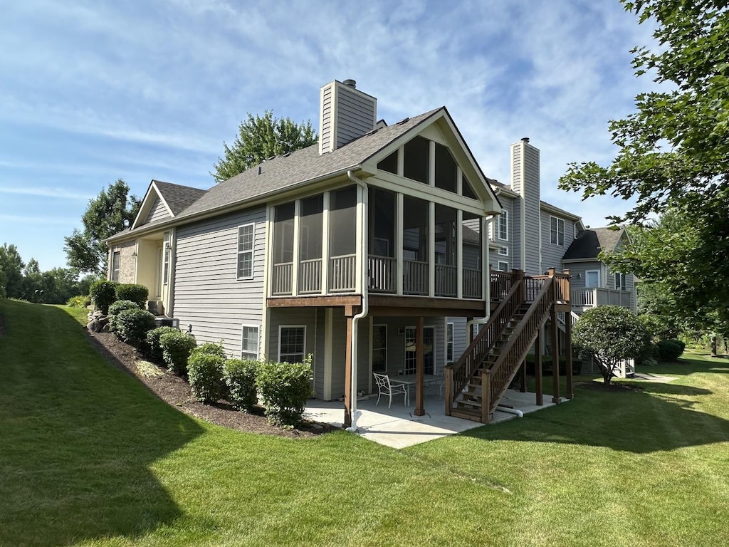 2017 Mallard Ln, Woodstock, IL 60098 - rear view of property featuring a chimney, a sunroom, a patio area, a lawn, and roof with shingles