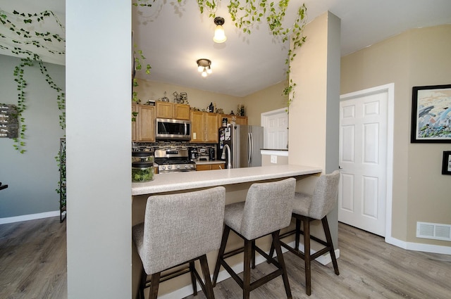 610 N Red Deer Rd, Round Lake, IL 60073 - kitchen featuring stainless steel appliances, light wood finished floors, a breakfast bar area, decorative backsplash, and light countertops